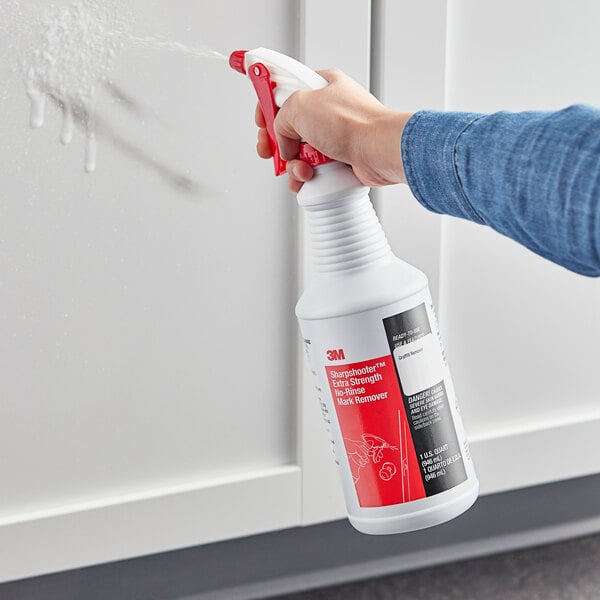 A person holding a white bottle of 3M Sharpshooter No-Rinse Mark Remover and spraying a white surface.