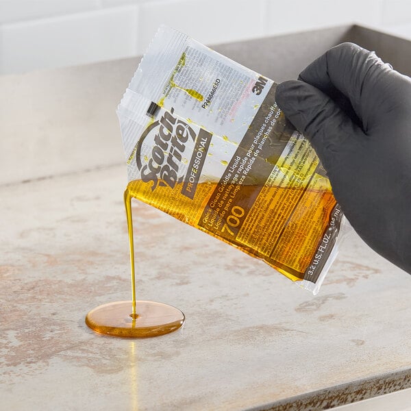 A packet of 3M Scotch-Brite liquid griddle quick clean being poured onto a griddle surface.