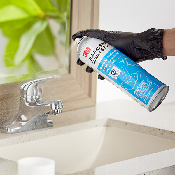 A hand in a black glove using 3M Stainless Steel Cleaner on a sink.