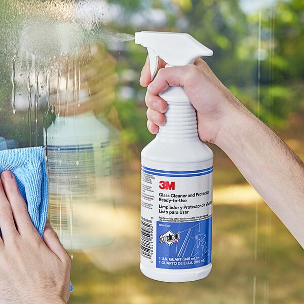 A hand using 3M Glass Cleaner to clean a window.