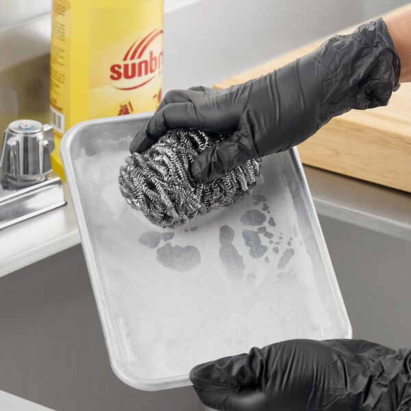 A stainless steel scrubber being used to clean a metal tray.