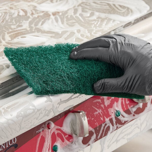 A green heavy-duty scouring pad being used to clean a soapy surface.