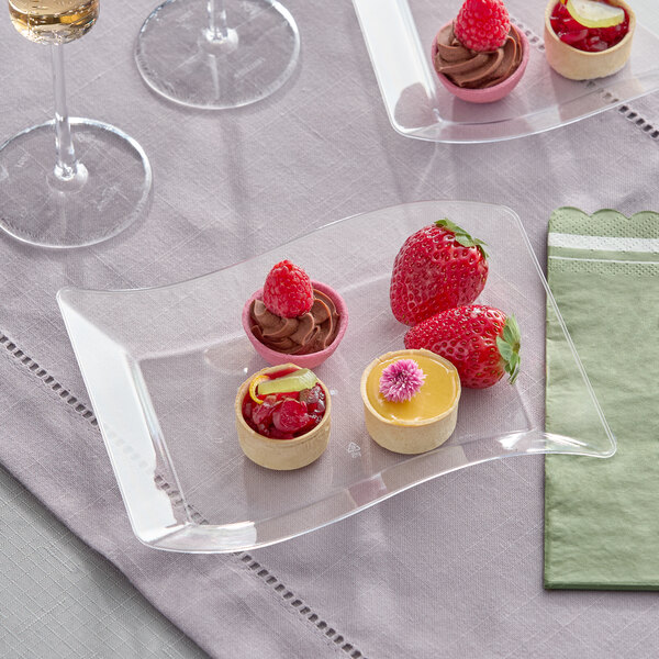 A clear plastic dessert plate with a wavy design, holding assorted small desserts and strawberries.