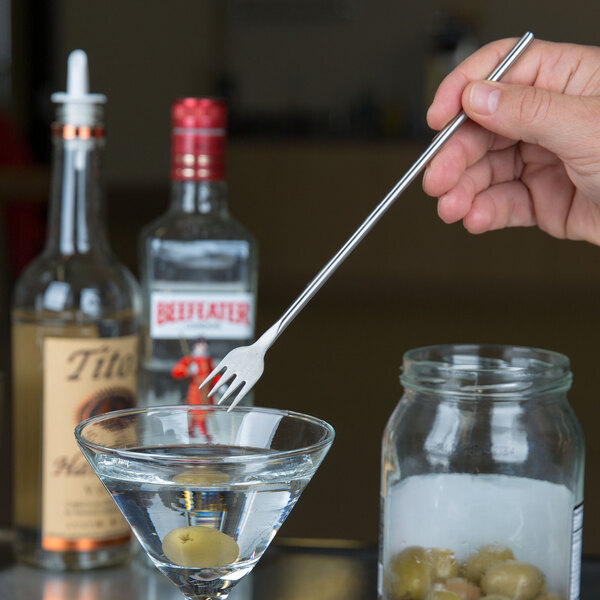 A hand holding an American Metalcraft stainless steel bar fork over a martini glass.