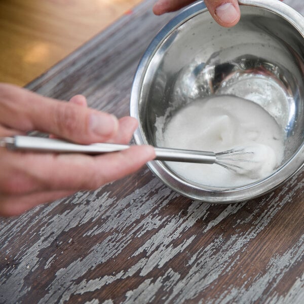 A person using an American Metalcraft stainless steel mini bar whisk to mix food in a bowl.