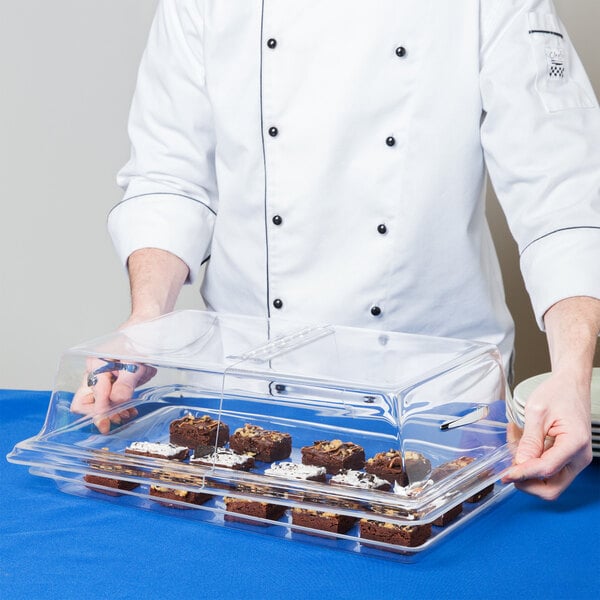 A person using a Cal-Mil clear rectangular bakery tray cover to display brownies.