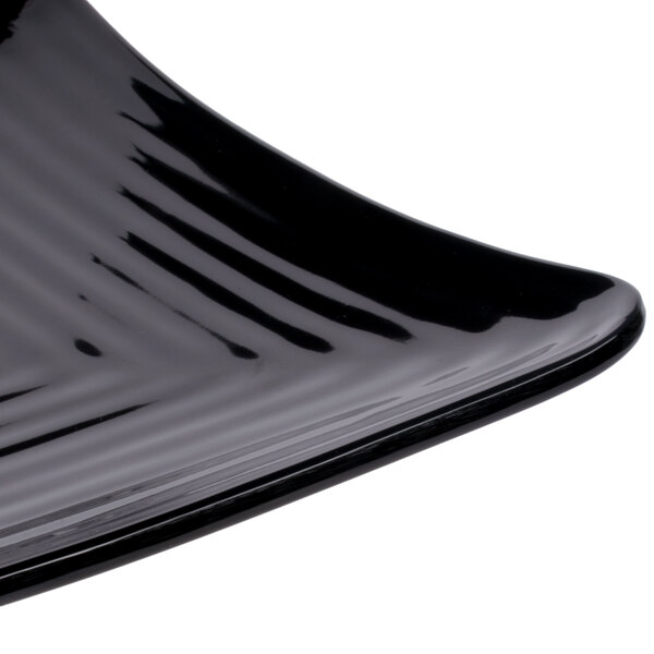 A close-up of a black GET Milano square plate with a curved edge.