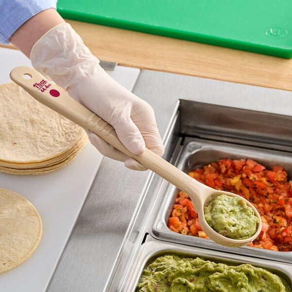 A person in gloves using a Carlisle long handle portion spoon to serve guacamole.