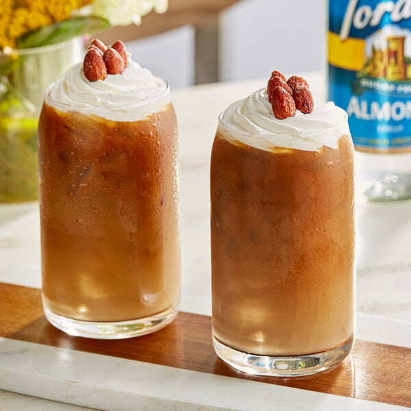 Two glasses of brown Torani Sugar-Free Almond flavored drinks with whipped cream and almonds.