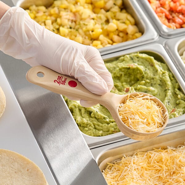 A person using a Carlisle beige and red Measure Misers portion spoon to serve shredded cheese.