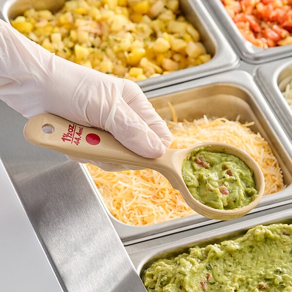 A gloved hand uses a Carlisle beige and red polycarbonate portion spoon to serve food.