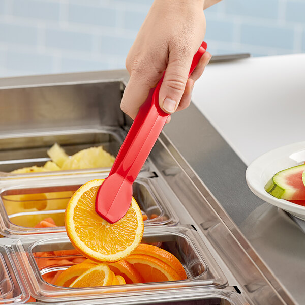 A person using red Cambro tongs to pick up an orange slice.