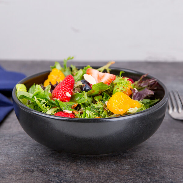 A black Hall China bistro bowl filled with fruit salad on a table.