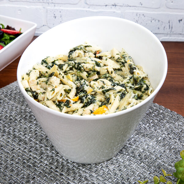 A 10 Strawberry Street white porcelain tall slant bowl filled with pasta, spinach, and cheese.