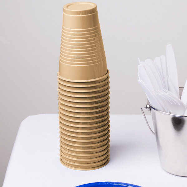 A stack of Creative Converting Glittering Gold plastic cups on a white surface.
