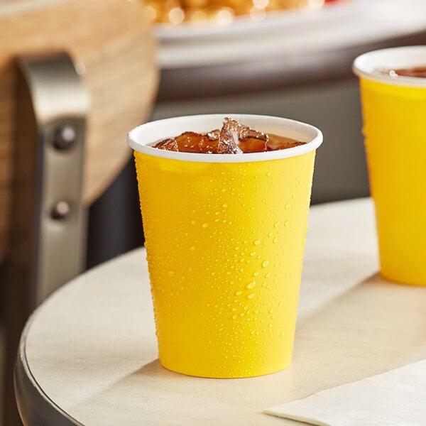 Two yellow Creative Converting School Bus Yellow paper cups with ice and drinks on a table.