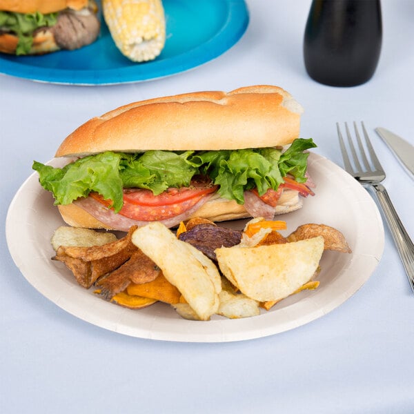 A sandwich with lettuce and tomato on an ivory paper plate with a fork.