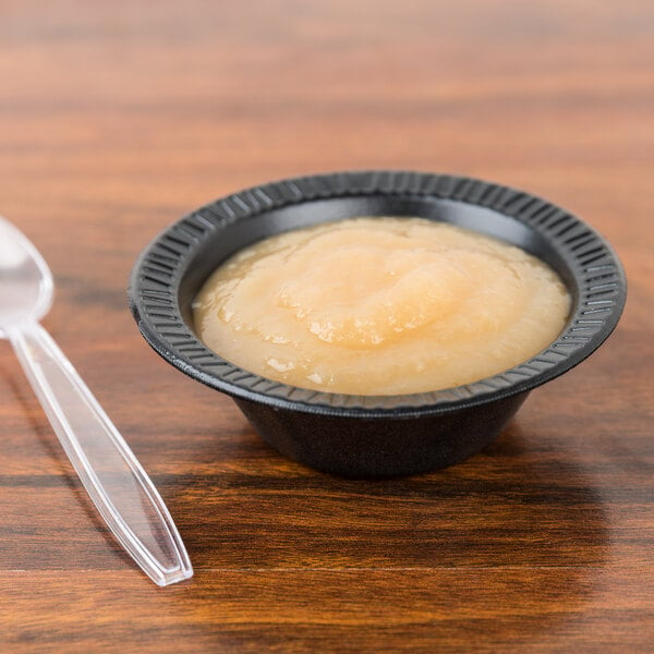 A Dart black laminated foam bowl filled with food on a table with a spoon.