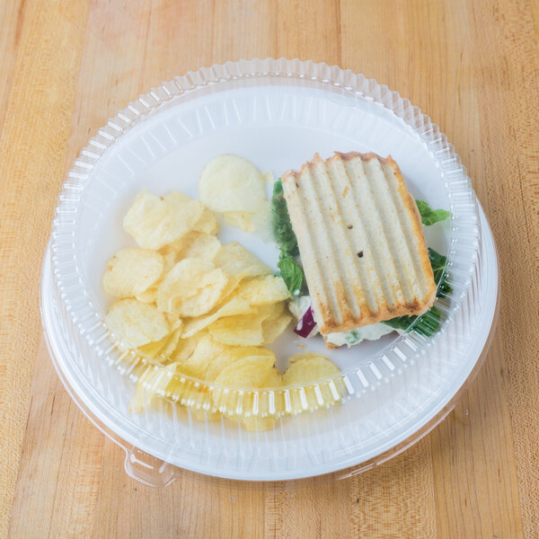 A Dart white foam plate with a sandwich and potato chips.