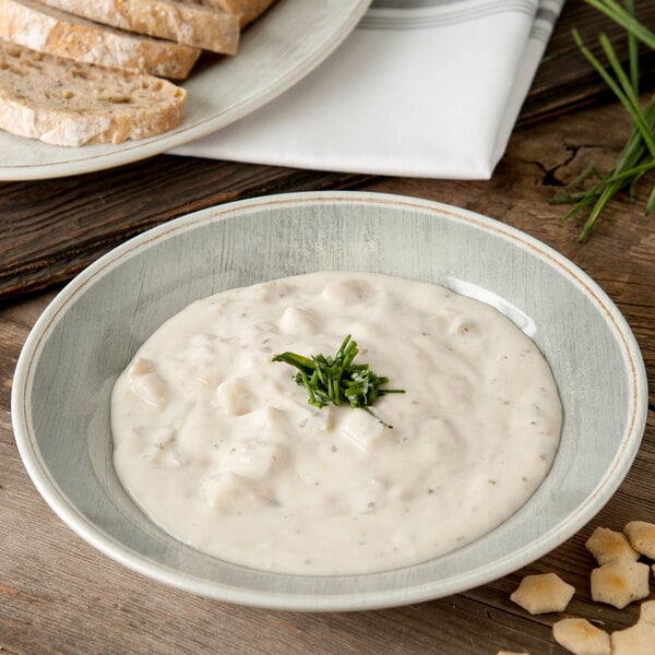 A Carlisle smoke melamine soup bowl filled with soup, next to a plate of bread with a green garnish.