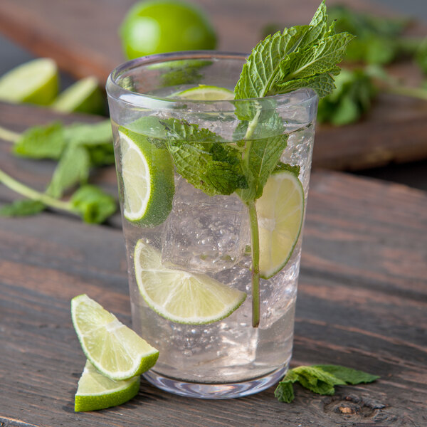 A Carlisle clear plastic beverage glass filled with water, ice, and lime slices.