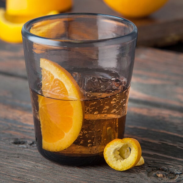 A Carlisle smoke plastic double rocks glass filled with liquid with a slice of orange.