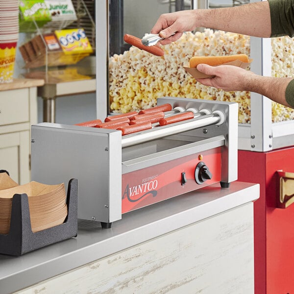 A man using an Avantco hot dog roller to cook hot dogs on a stadium concession stand counter.