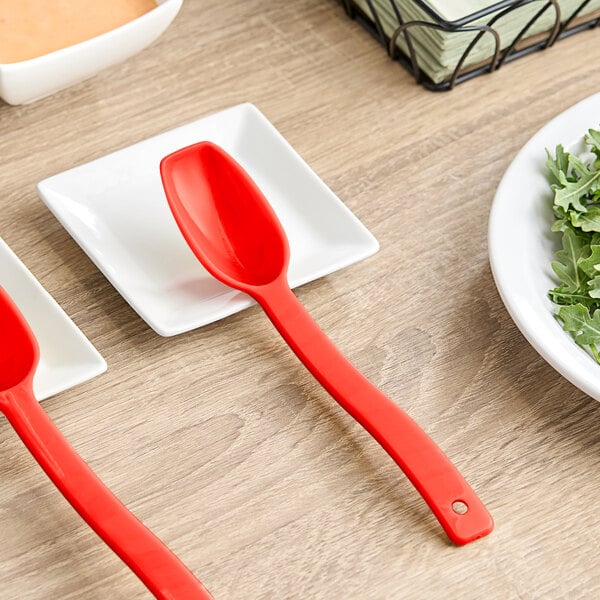 Two red Cambro Camwear salad bar spoons on a white plate with salad