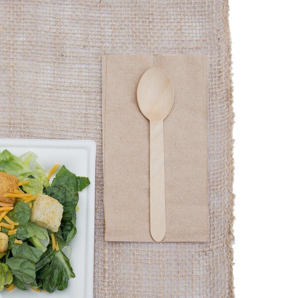 Wooden spoon on kraft napkin next to sugarcane plate with salad