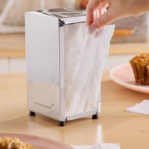 A metal napkin dispenser holding tall-fold white napkins on a table.