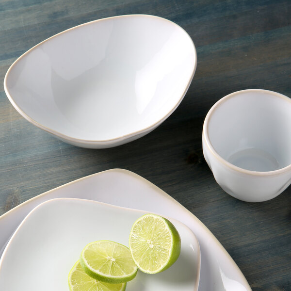 A Tuxton white china bowl with a gold rim filled with limes.