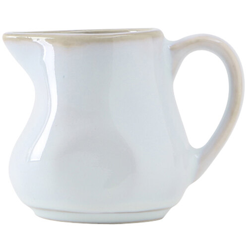 A white Tuxton China creamer with a handle.