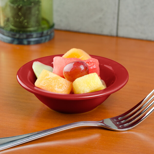 A Tuxton Cayenne Colorado fruit bowl filled with fruit on a table with a fork.