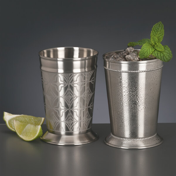 Two World Tableware stainless steel mint julep cups filled with ice and mint next to a lime wedge.