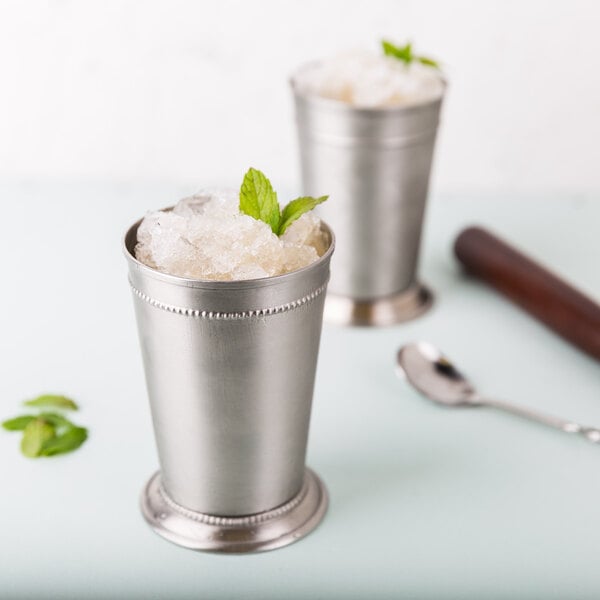 Two silver World Tableware stainless steel mint julep cups with ice in one