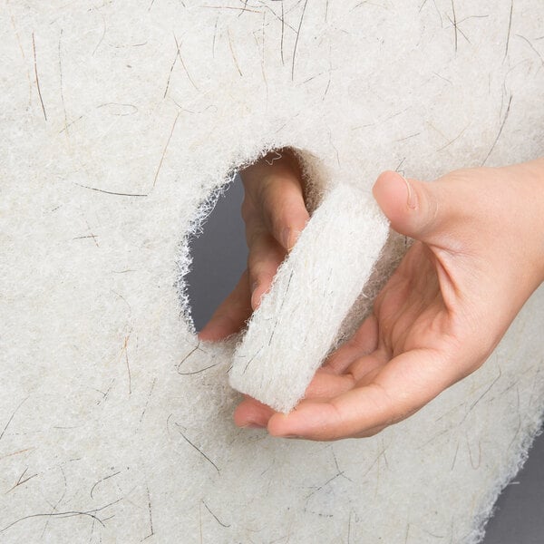 A white 13-inch round floor polishing pad with a hole in the center, shown being handled.