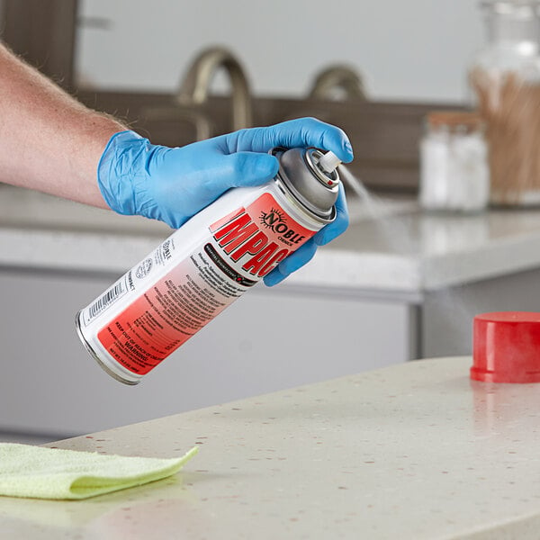 A person wearing blue gloves holding a Noble Chemical spray can and spraying it.