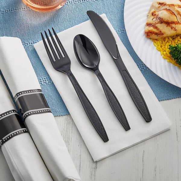 Black plastic cutlery with a fork, spoon, and knife on a white napkin.