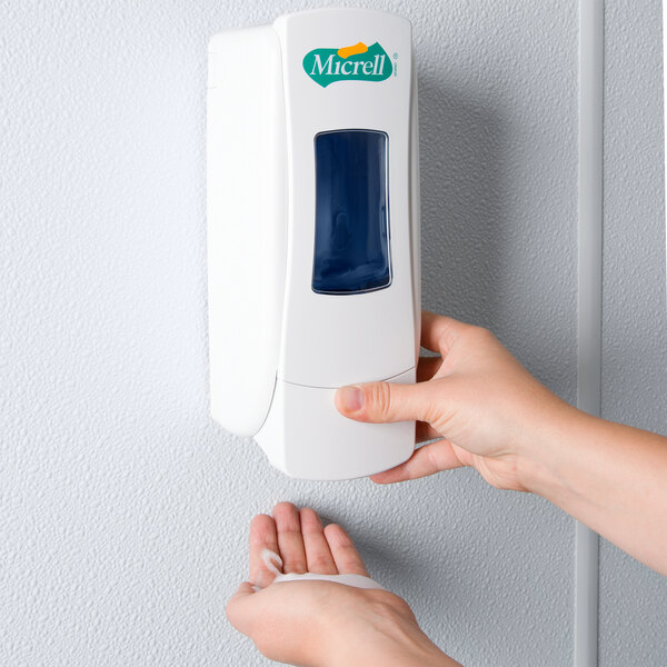 A person using a Micrell manual soap dispenser on a wall.