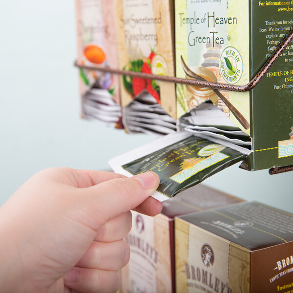 A hand taking a box of Bromley tea out of a rack.