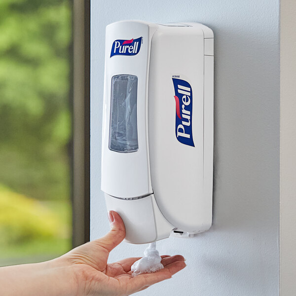 A person's hand using a Purell hand sanitizer dispenser.