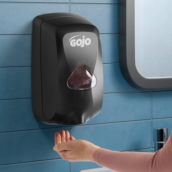 A black GOJO TFX 1200 mL touchless hand soap dispenser mounted on a blue tiled wall.