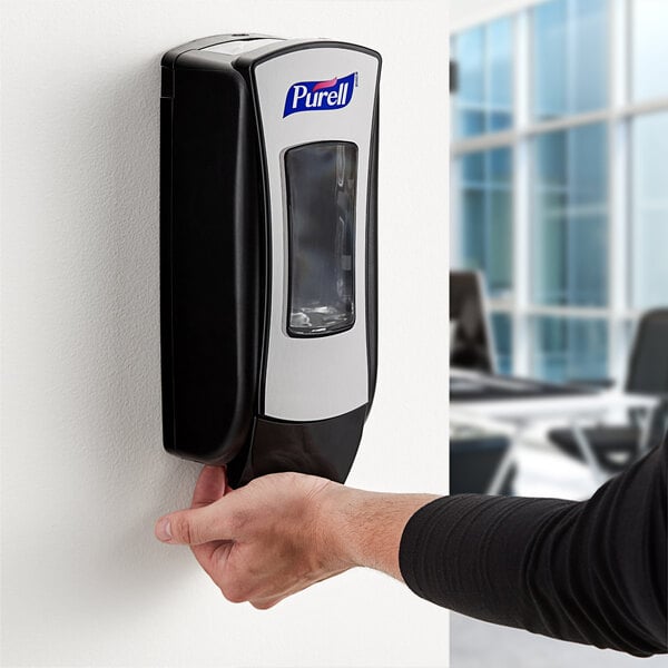 A person using a Purell black manual hand sanitizer dispenser.