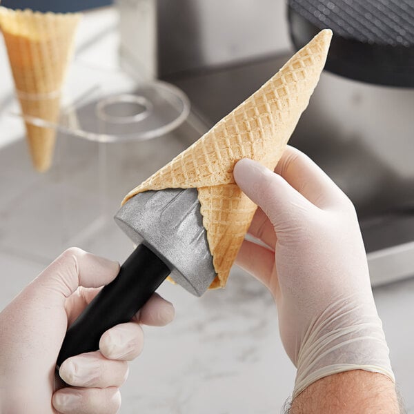 A hand holding a waffle cone using a Carnival King Waffle Cone Mandrel with a black and yellow handle.