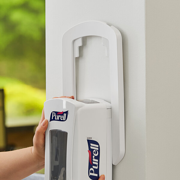 A hand holding a white GOJO True Fit wall plate over a white soap dispenser.