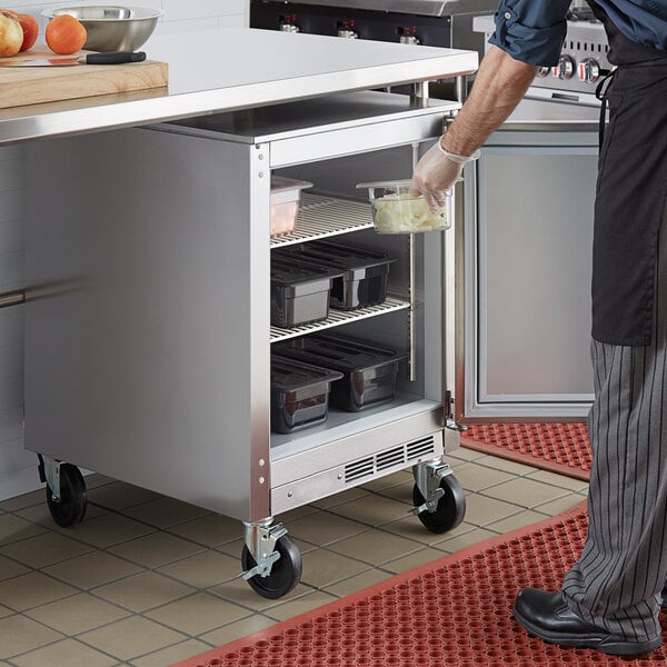 A man opening a Beverage-Air undercounter refrigerator in a school kitchen to put food away.