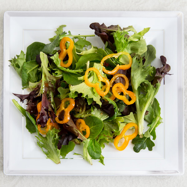 A Fineline white plastic square plate with a salad and a yellow bell pepper slice.