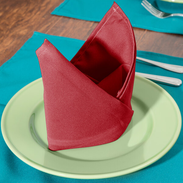 A folded red Intedge cloth napkin on a plate.