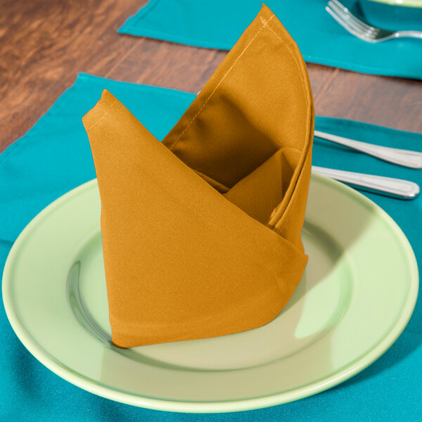 A folded gold Intedge cloth napkin on a plate with silverware.