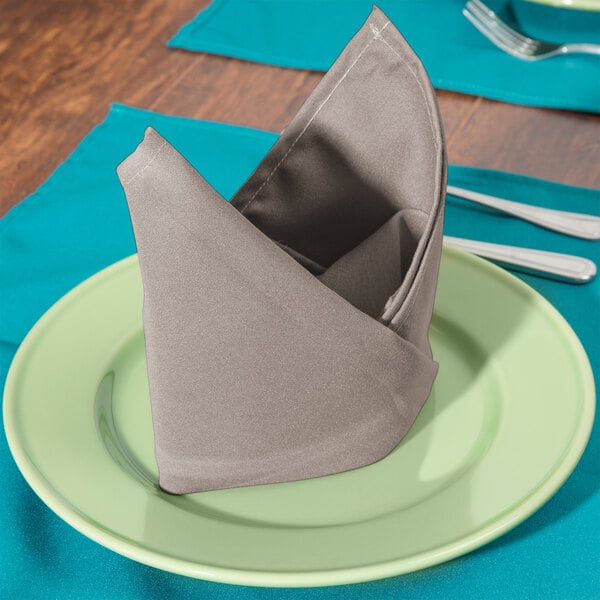 A folded beige Intedge cloth napkin on a plate with a fork.